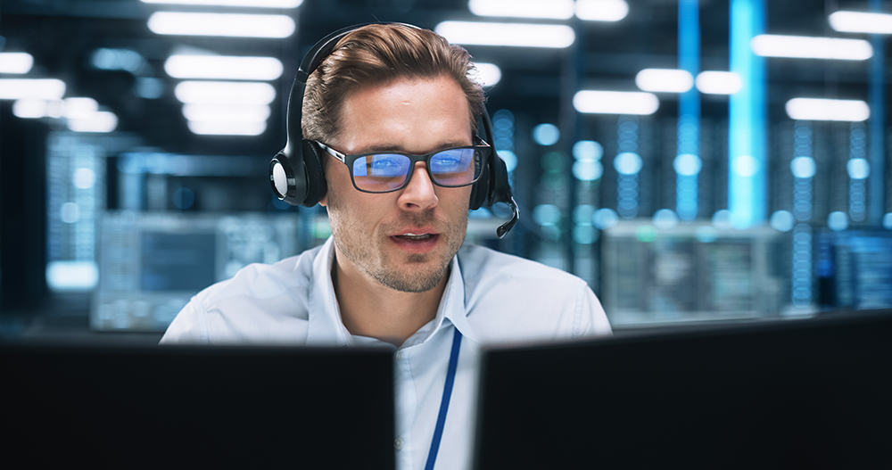 Man with headset behind 2 computer monitors